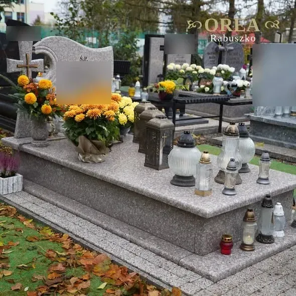 Pomnik grobowcowy z brązowego granitu z krzyżem z metaloplastyki, otoczony zniczami i chryzantemami