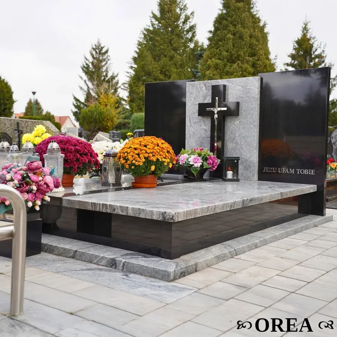 Nagrobek z jasnego granitu Viscont White w czarnej ramie Monumental, z czarnym krzyżem i metalowym krucyfiksem na cmentarzu